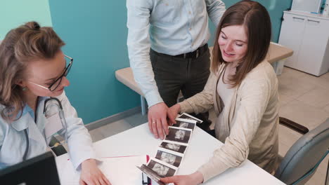 vista superior del ginecólogo que muestra imágenes de ultrasonido a su paciente embarazada y a su esposo en consulta médica