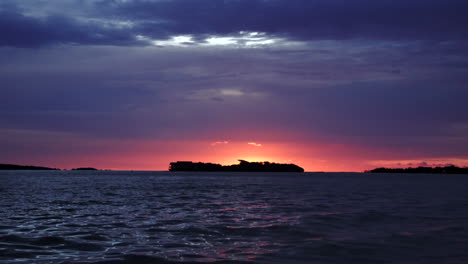 Handshot of intense colors sunset on sea hided island with birds flying above