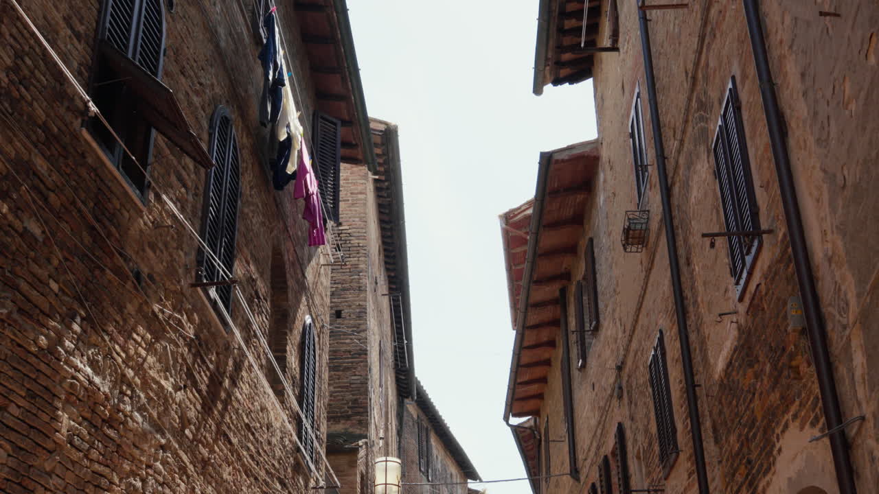 Antichi edifici in mattoni fiancheggiano uno stretto vicolo in Toscana, con panni stesi ad asciugare
