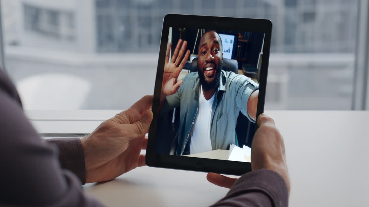 Primo piano di un manager sorridente che chatta tramite webcam con un collega di una startup usando un tablet in ufficio