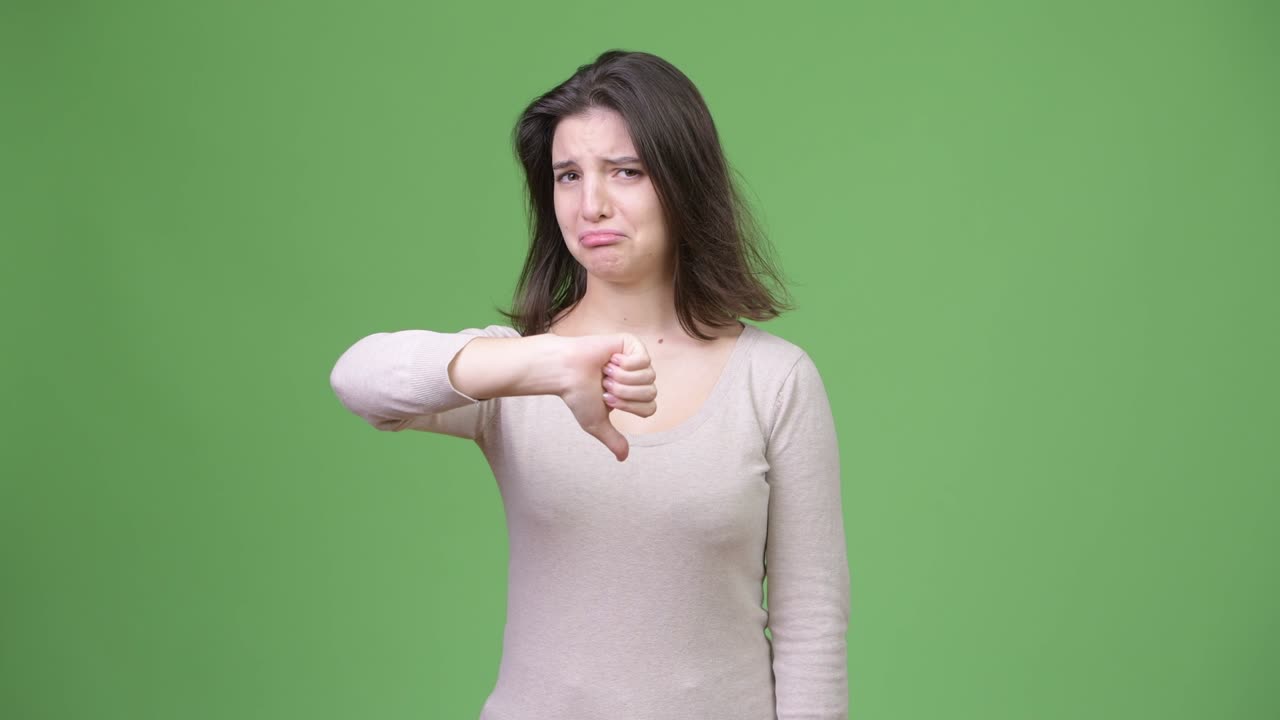 Young sad woman giving thumbs down against green background