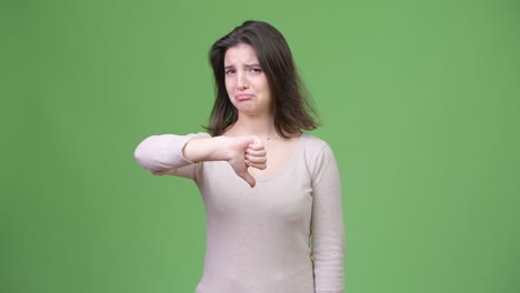 young sad woman giving thumbs down against green background