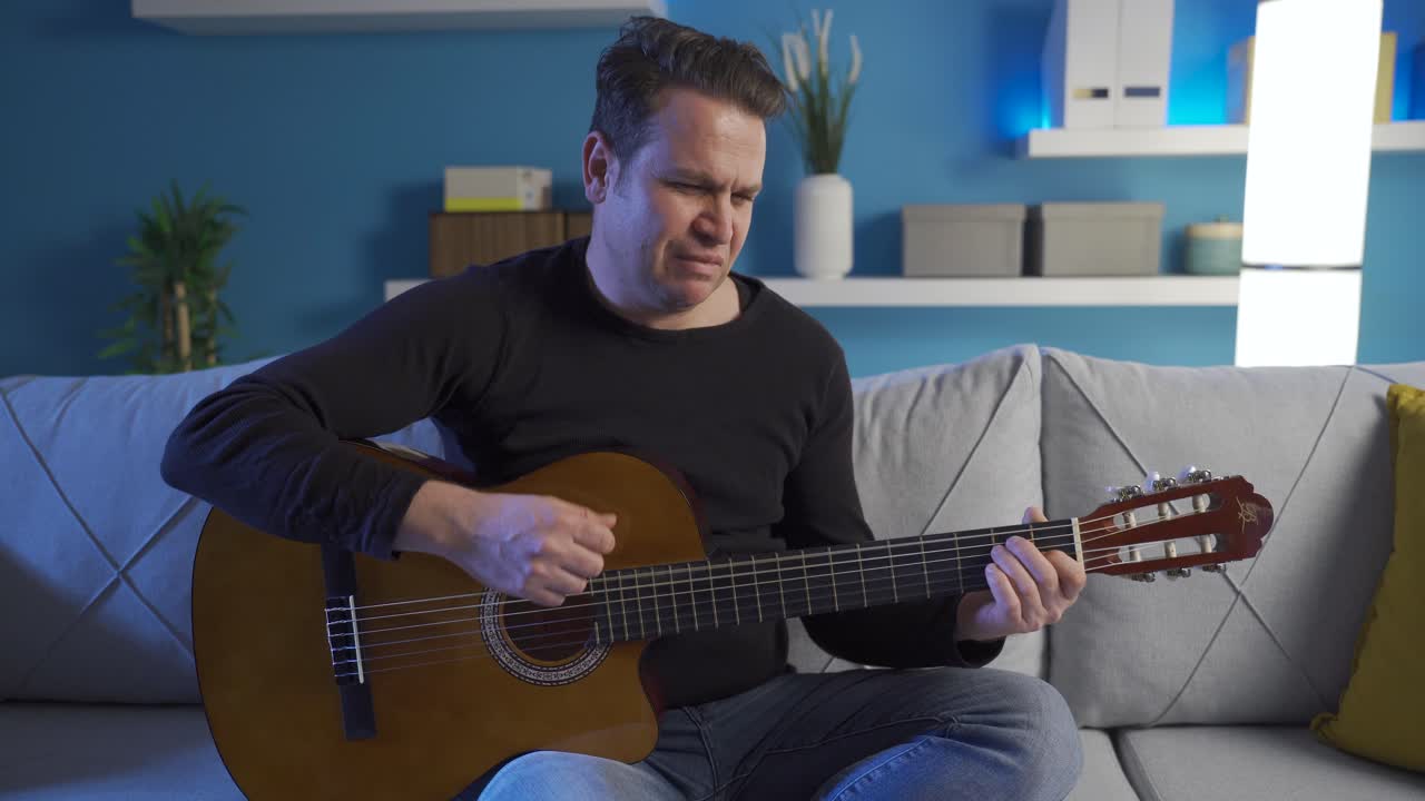 불행하고 우울한 남자가 집에서 혼자 기타를 연주하고 있습니다.