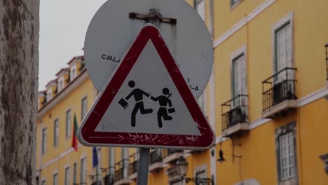 Portugiesisches-Verkehrsschild-Mit-Gelbem-Gebäude-Dahinter-In-Lissabon,-Portugal