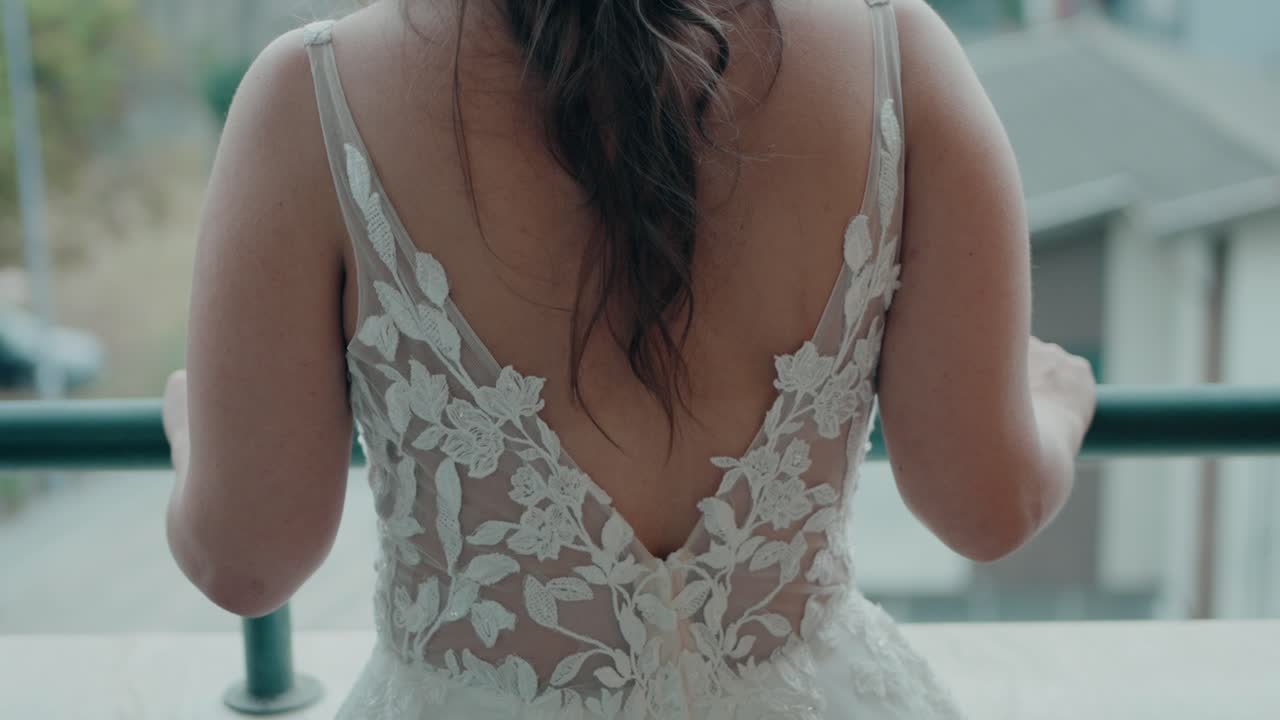 Bride in a lace gown outside on a balcony, showing the elegant back design