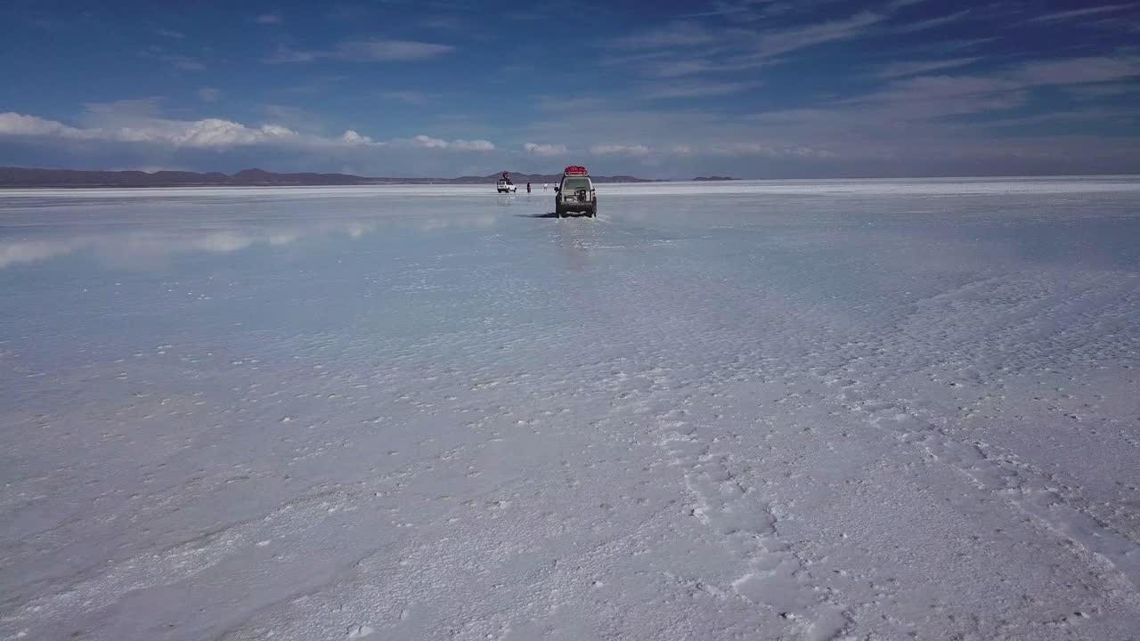 Pengambilan gambar dari perspektif belakang sebuah kendaraan yang melaju melintasi Dataran Garam Bolivia.