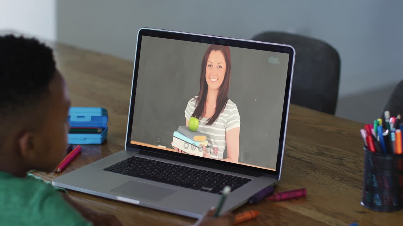 niño afroamericano haciendo la tarea mientras tiene una videollamada con una maestra en una computadora portátil en casa