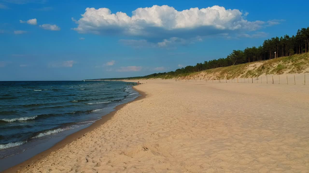 Ujęcie z lotu ptaka na pustą plażę, wydmę i Morze Bałtyckie.