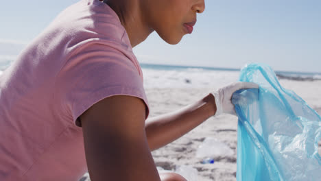 mujer afroamericana recogiendo desechos plásticos en la playa
