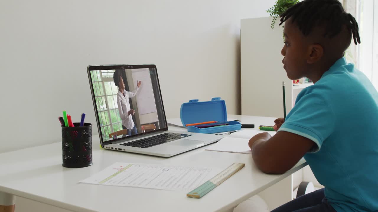 African american boy doing homework while having a video call with female teacher on laptop at home