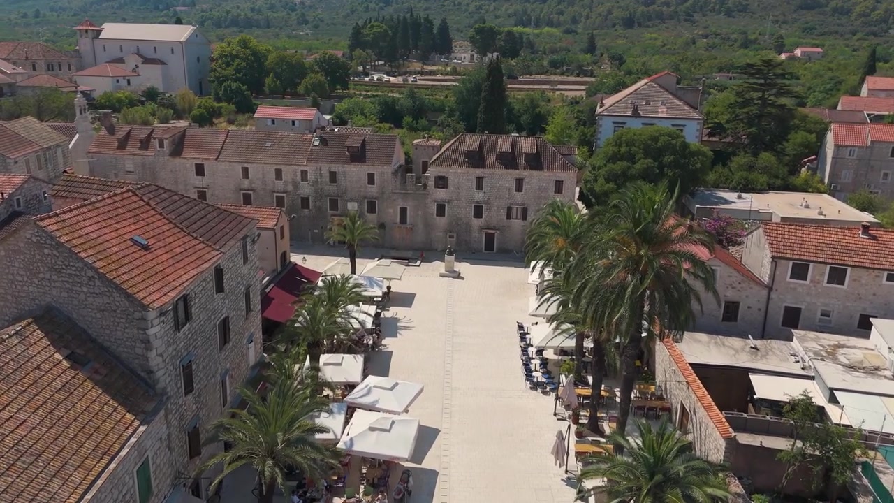 La storica piazza di Stari Grad è incorniciata da vecchie case, caffè all'aperto e alte palme in una luminosa giornata estiva.