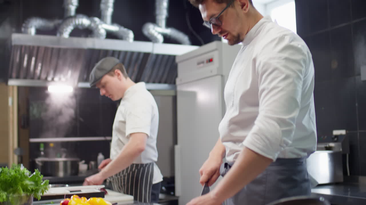 Chef Cutting Tomato and Talking to Colleague in Kitchen