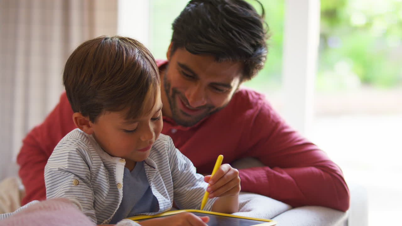 padre e hijo en casa en el sofá en la sala de estar jugando con el juego de dibujo juntos