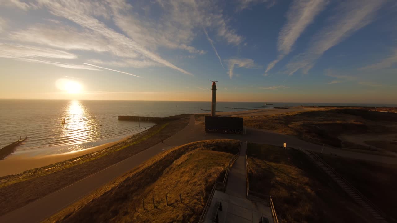 Aerial shot of the dunes and dykes flying towards a radar tower during golden hour