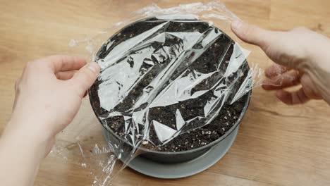 covering a pot of soil with plastic wrap to help seeds sprout indoors