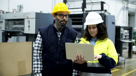 ingenieros confiados discutiendo el trabajo mientras están de pie con la computadora portátil