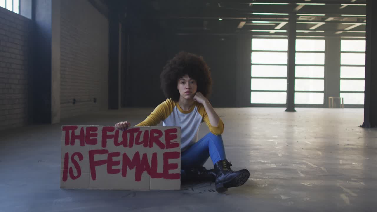 retrato de una mujer afroamericana con un cartel de protesta en un garaje vacío