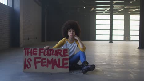 Portrait-of-african-american-woman-holding-protest-placard-in-empty-parking-garage