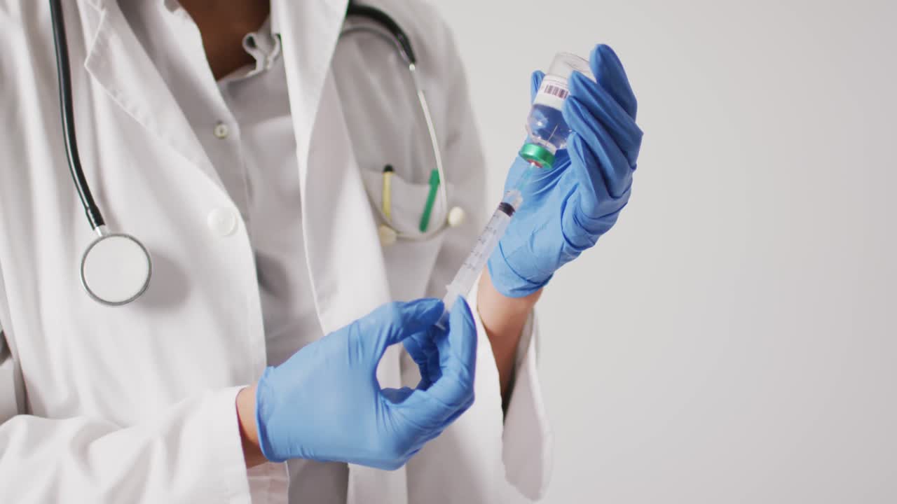 video de una doctora biracial sosteniendo un vial de vacuna sobre un fondo blanco