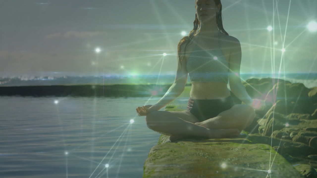 Meditating by ocean, woman surrounded by digital network animation, feeling calm