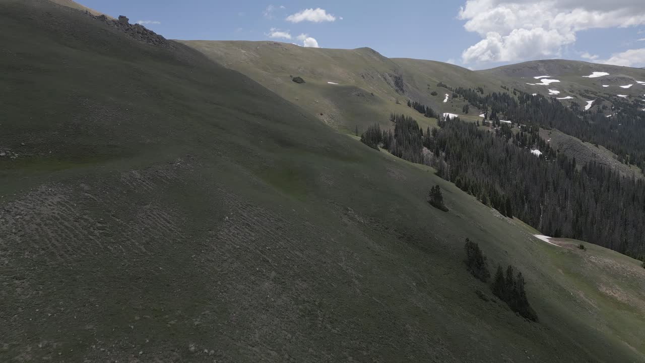 aerial sigue la pendiente de hierba estéril hacia las manchas de nieve de la cresta de la cumbre