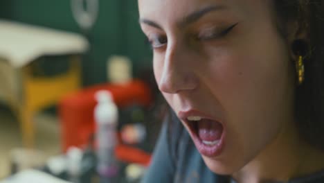 primer plano de una hermosa chica joven con grandes pendientes y maquillaje que se centra en tatuar en su estudio y guiña la cámara en cámara lenta