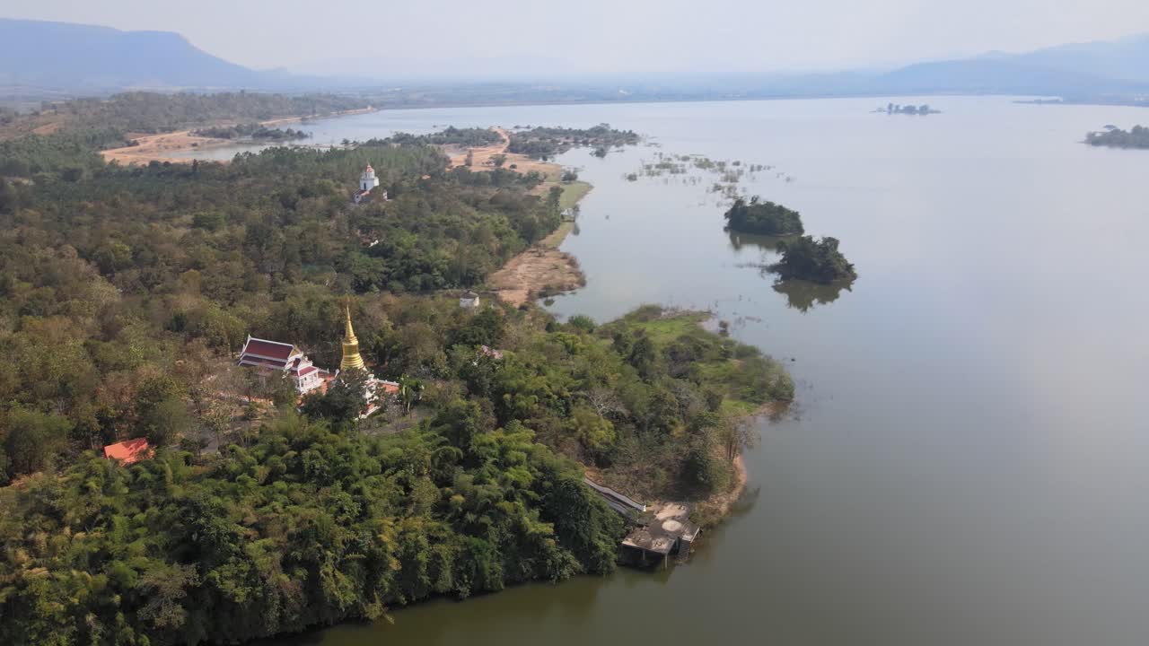 Aerial View of Wat Wang Phu Sai Temple on a Hilltop Surrounded by Trees Next to a Lake.
