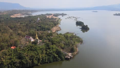 aerial view of wat wang phu sai temple on a hilltop surrounded by trees next to a lake.