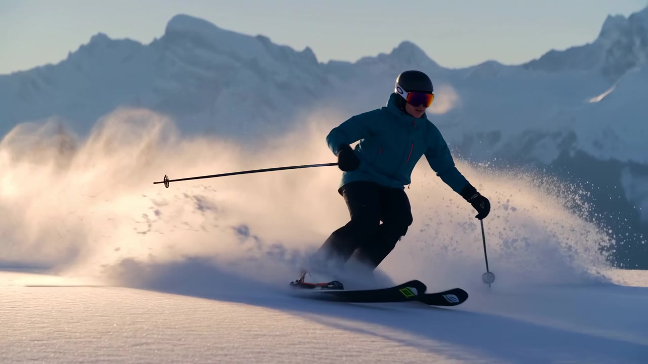 Sciatore con casco e abbigliamento invernale si inclina aggressivamente in una curva scolpita su un pendio montano innevato e illuminato dal sole, spruzzando una nuvola di polvere a forma di arco. Alberi di conifere