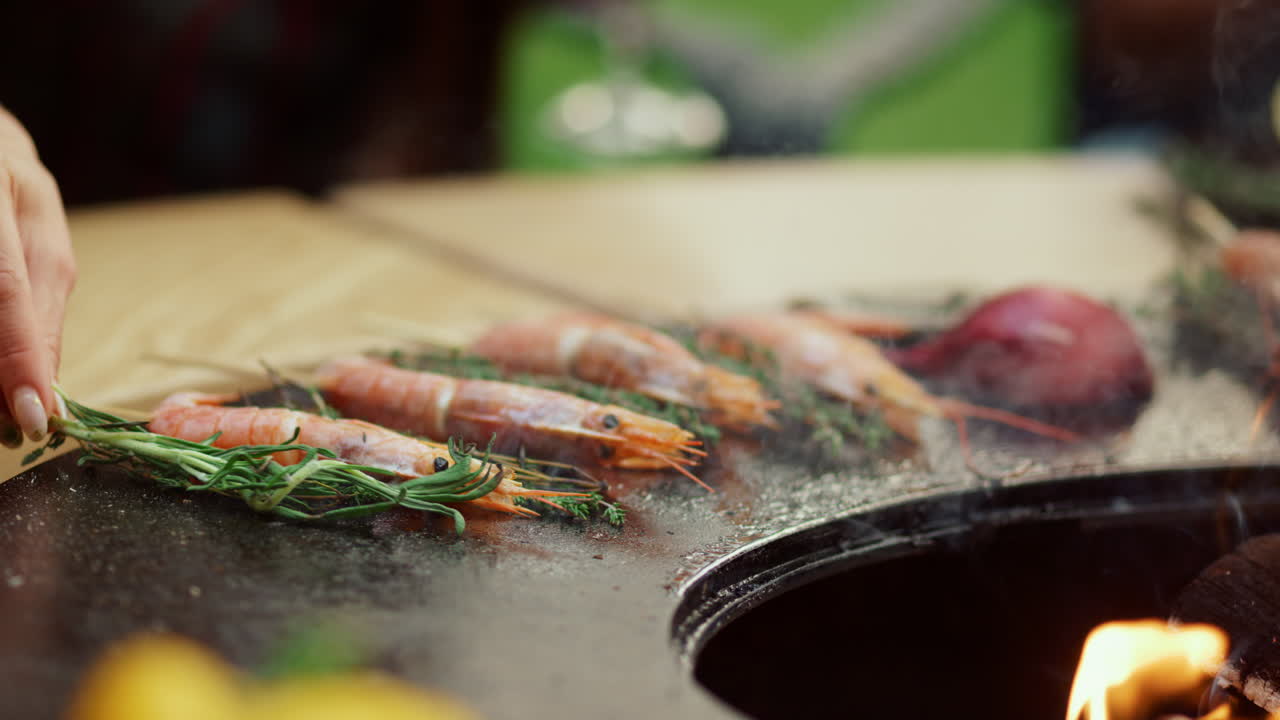 알 수 없는 여자가 바비 ⁇  그릴에 허브를 넣고 있다. 바 ⁇ 에 그릴에 새우를  ⁇ 고 있다.