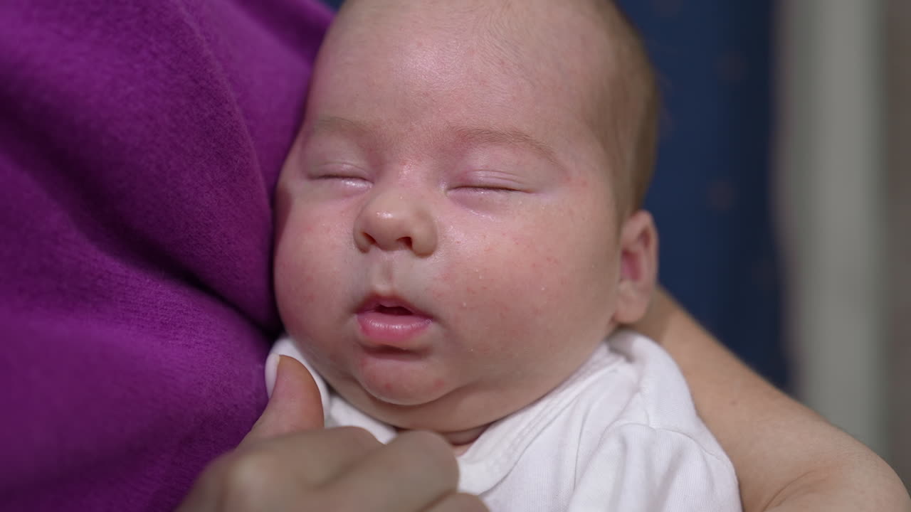 Face of an infant baby sleeping deeply and doesn't want to wake up. Loving mum trying to wake her kid up and touches his sweet cheeks tenderly. Close up.