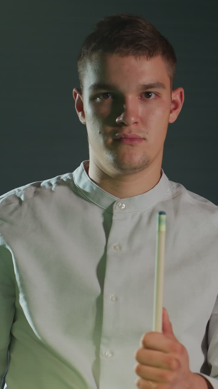 vista frontal de un joven con camisa blanca contra un fondo oscuro sosteniendo el taco cuidadosamente, aplicando la cubierta roja con una expresión enfocada. la iluminación cálida destaca la concentración