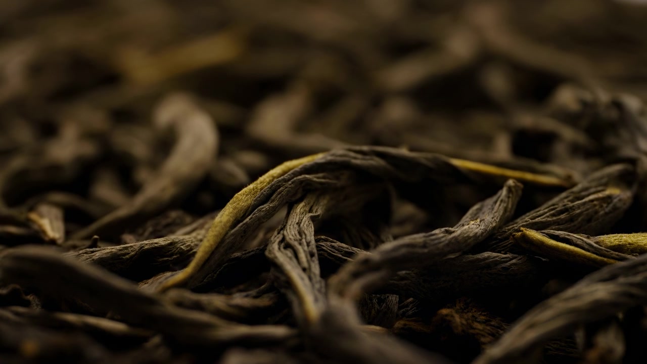Close-up view of loose dried tea leaves reveals layered textures, curled shapes, and muted earthy colors across a dark surface with gentle illumination and shallow depth