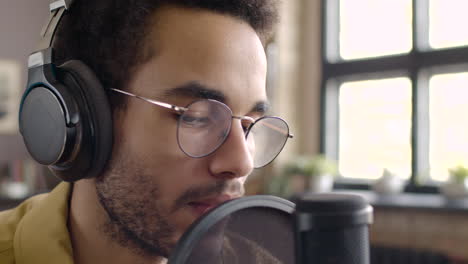 vista de cerca del hombre grabando un podcast usando anteojos y auriculares y hablando en un micrófono