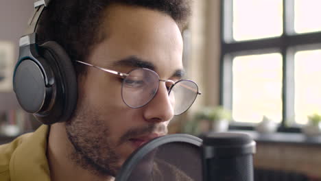 close up view of man recording a podcast wearing eyeglasses and headphones and talking into a microphone