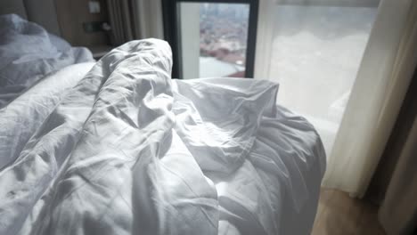 unmade bed in hotel room with city view