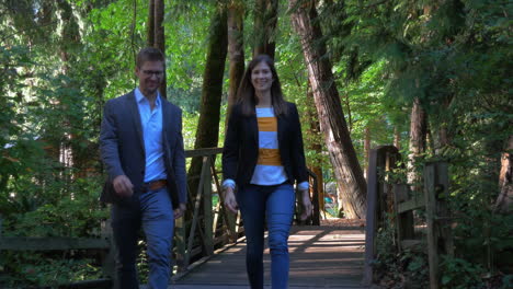 savvy young, good looking business professionals walk towards camera in a park over a beautiful shaded wooden bridge outside in nature on a sunny day.