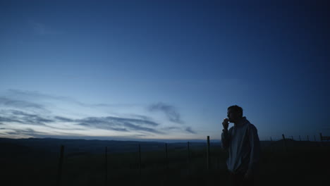 hombre solo al aire libre por la noche enciende cigarrillos, fuma mirando el paisaje rural