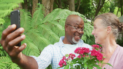 happy senior diverse couple wearing shirts and taking selfie with smartphone in garden