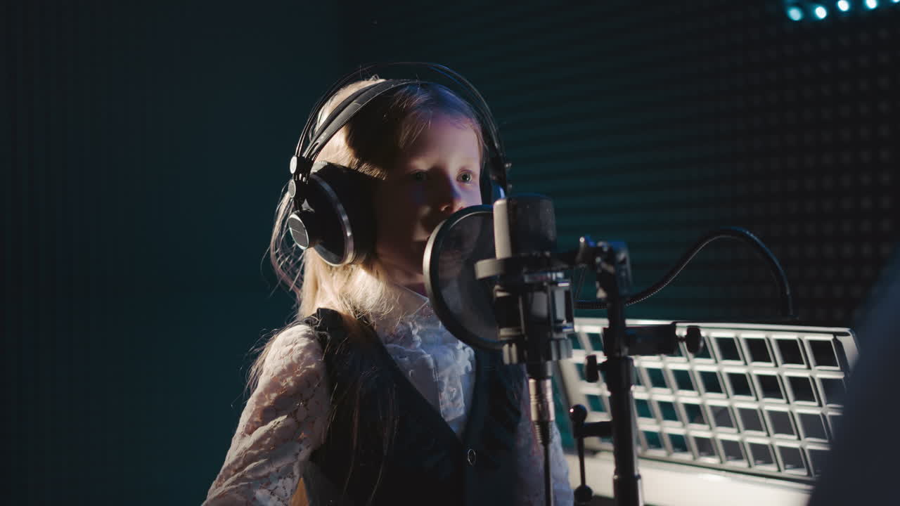 Young girl rehearses singing closeup. Gifted blonde child wearing headphones demonstrates vocal abilities in recording studio. Talented kid performs song