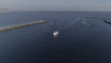 Aerial-shot-flying-towards-a-white-vessel-heading-into-the-Newport-Bay-with-birds-flying-around-it-in-Newport-Beach,-California