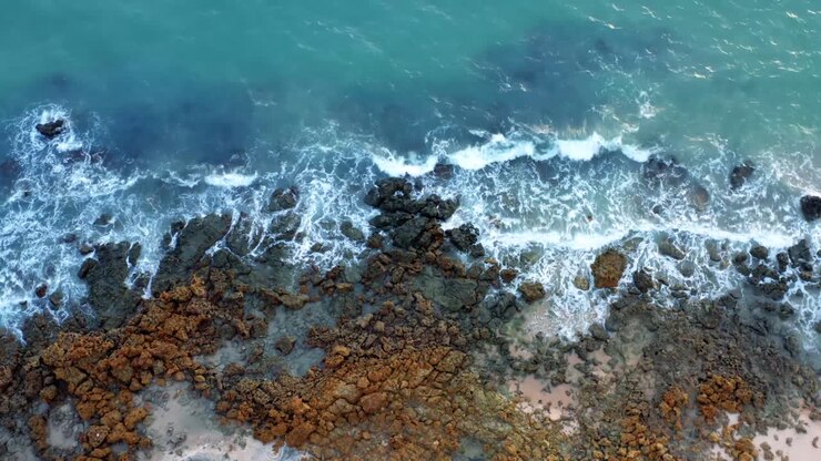 Splendida vista aerea in ascesa delle onde dell'oceano che si infrangono sulle rocce sulla costa di una spiaggia tropicale del Brasile settentrionale chiamata Tabatinga, con acqua blu e sabbia dorata, vicino a João Pessoa in una calda giornata estiva