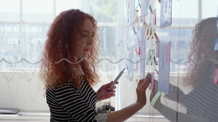 Female holding marker, studying sketches and arranging sticky notes on clear glass, refining design