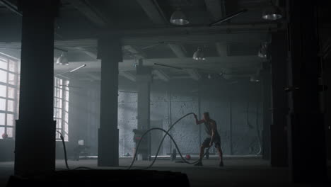 guy battling ropes in gym. athletic man doing crossfit workout in loft building