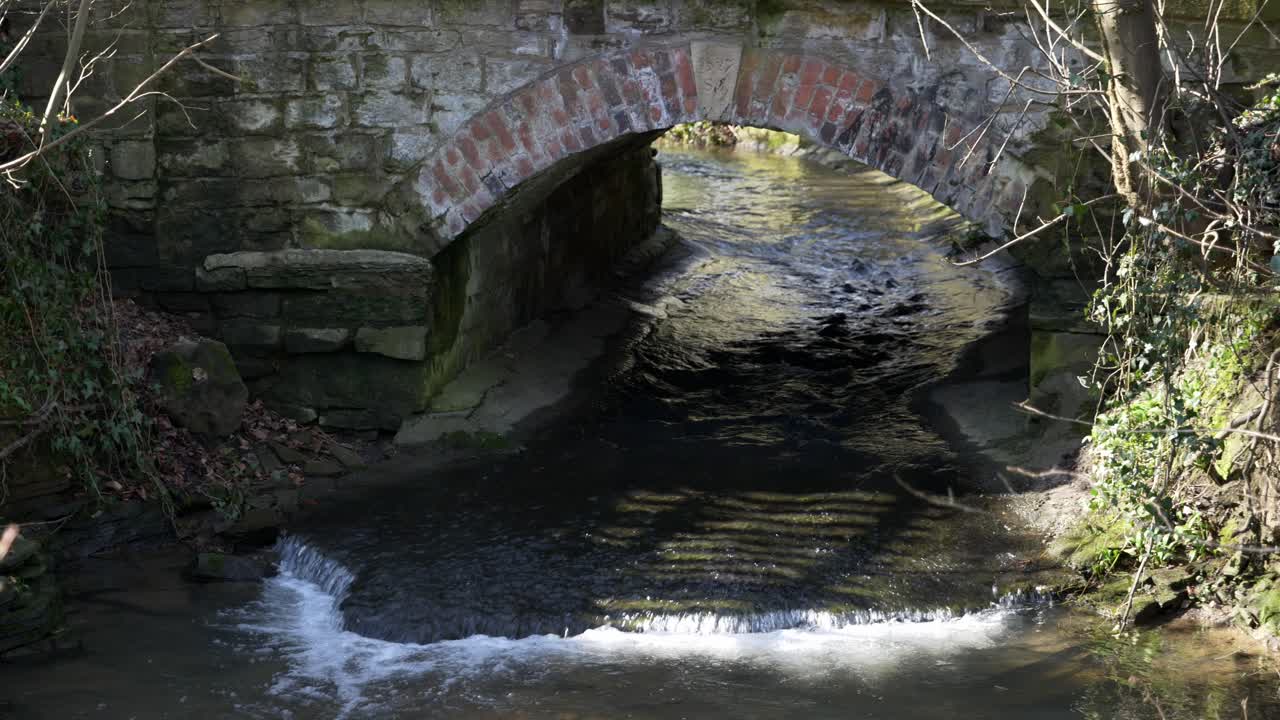 agua que fluye bajo un pequeño puente de piedra y ladrillo