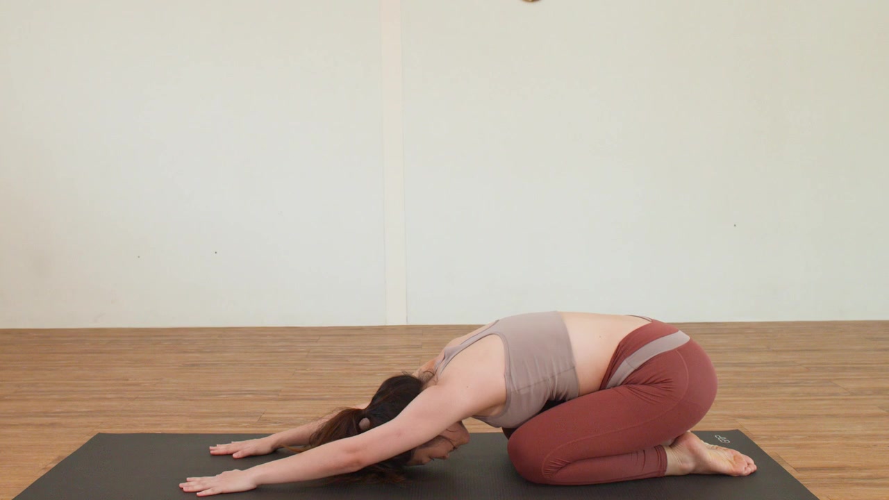 Giovane donna esegue l'allungamento Balasana su un tappetino in un ambiente di studio minimalista