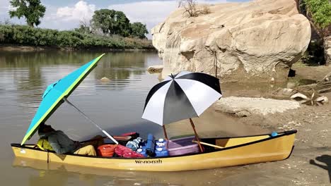 guy relaxing under umbrella in canoe on river banks in utah