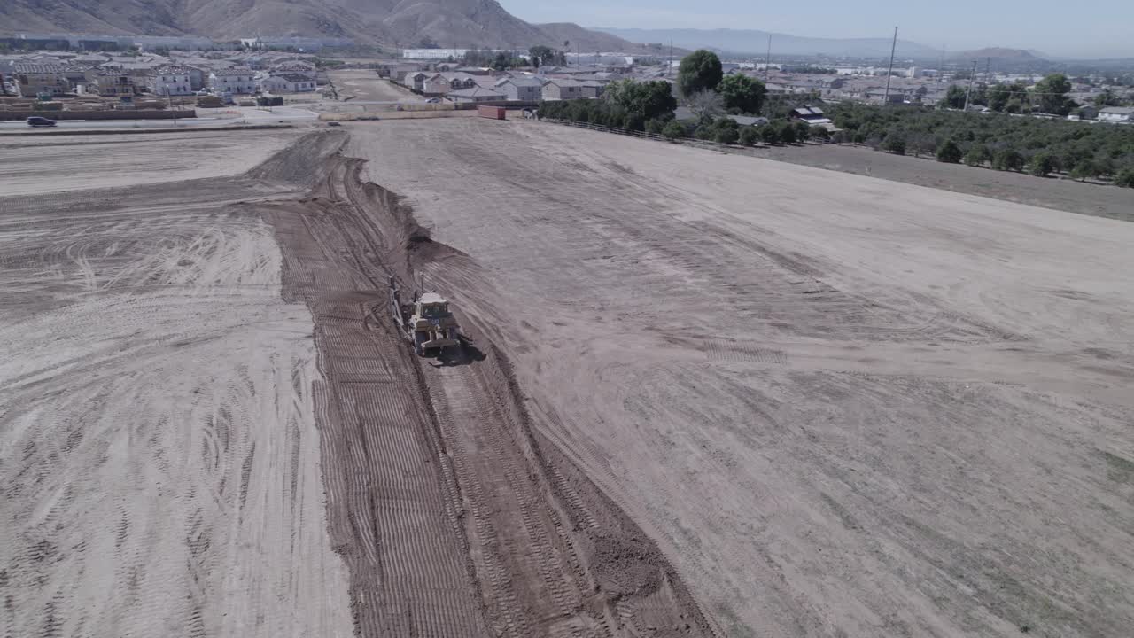 un avión no tripulado observa un cargador de pista moviendo la tierra de manera eficiente, preparando hábilmente el terreno para el inicio de una nueva construcción de viviendas