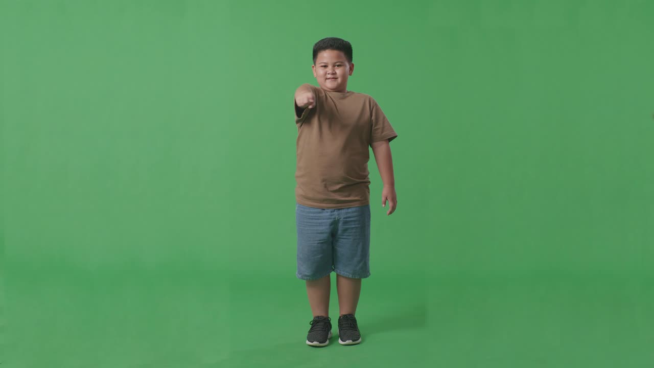 cuerpo lleno de niño asiático sonriendo y haciendo un gesto honesto en el fondo de la pantalla verde en el estudio