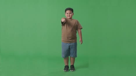 cuerpo lleno de niño asiático sonriendo y haciendo un gesto honesto en el fondo de la pantalla verde en el estudio